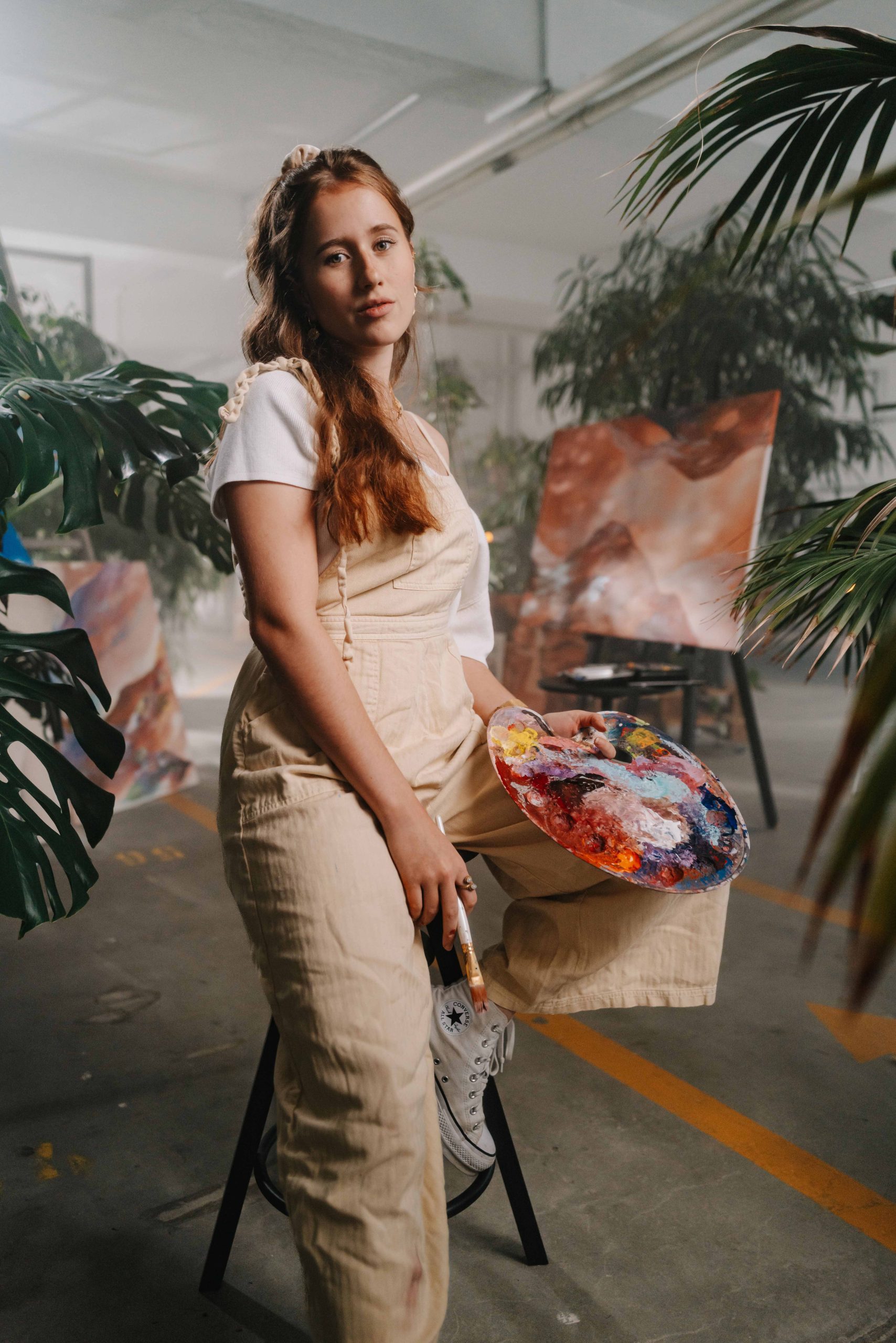 This photography was taken on a job for Stabilo, a pen manufacturer based near Nürnberg. The model is sitting on a chair with painting gear in her hands. She is sitting in a room full of plants and paintings looking straight into the camera.